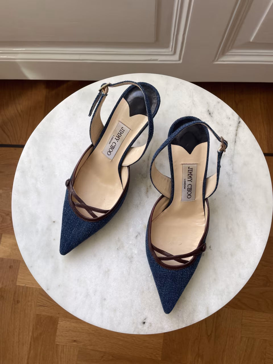 Luxury jimmy choo london pointed-toe slingback shoes in dark blue denim with brown leather trim on white marble surface featured in losangiqué